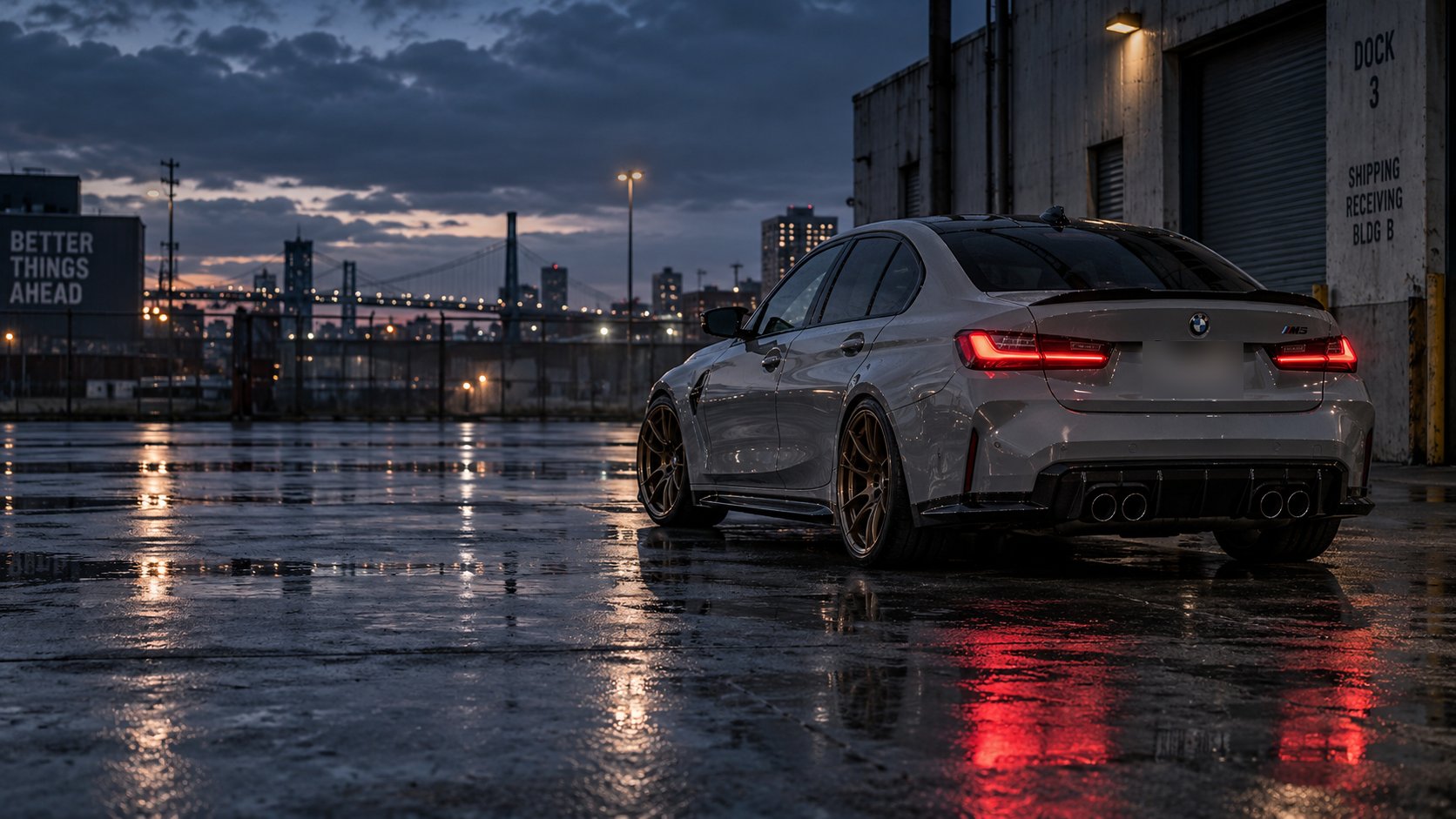Grey BMW G80 M3 on bronze wheels in a wet industrial lot at dusk